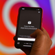An image of the prompt to create a Reel on Instagram is shown on a phone. The Instagram logo can be seen in the background.